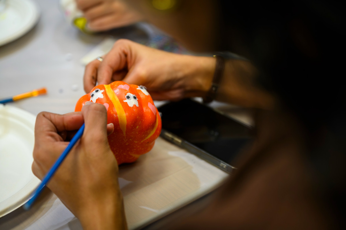 A student decorates her small orange pumpkin with mini, white painted ghosts, complete with googly eyes.