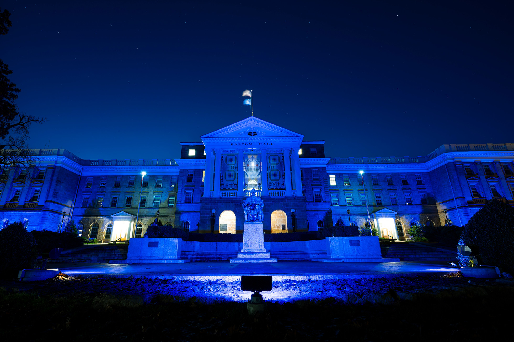 The front exterior of Bascom Hall, lit up with blue lights at night. 