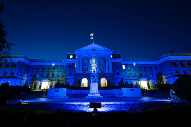 The front exterior of Bascom Hall, lit up with blue lights at night.