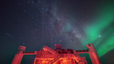 A view of the IceCube Lab with a starry night sky showing the Milky Way and green auroras.