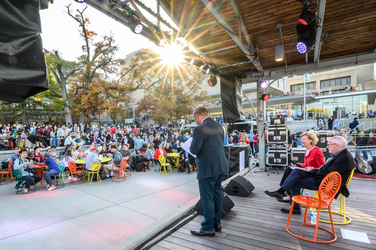 Interim Chancellor Eric Wilcots giving remarks on an outdoor stage with U.S. Senator Tammy Baldwin and Nobel Laureate Francis Halzin on a sunny day