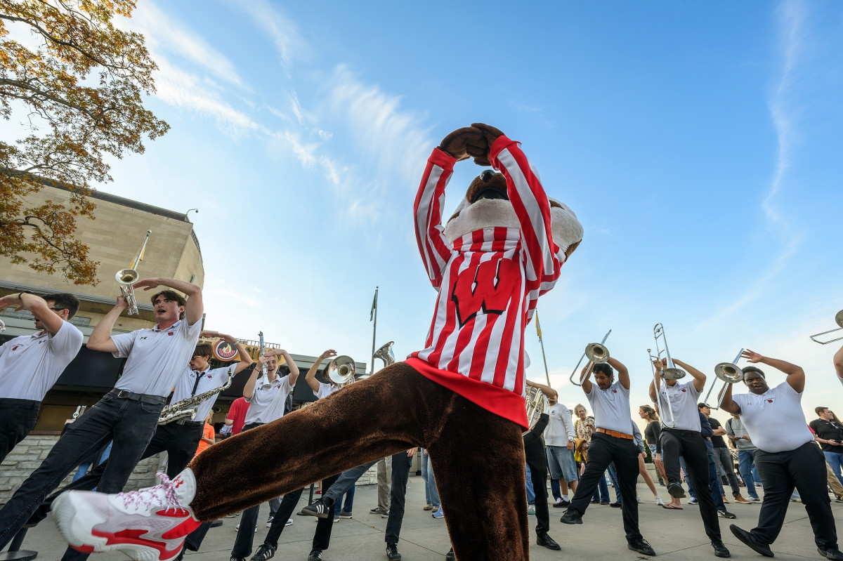 Bucky Badger mascot dancing with UW–Madison band members outdoors with a blue sky in the background