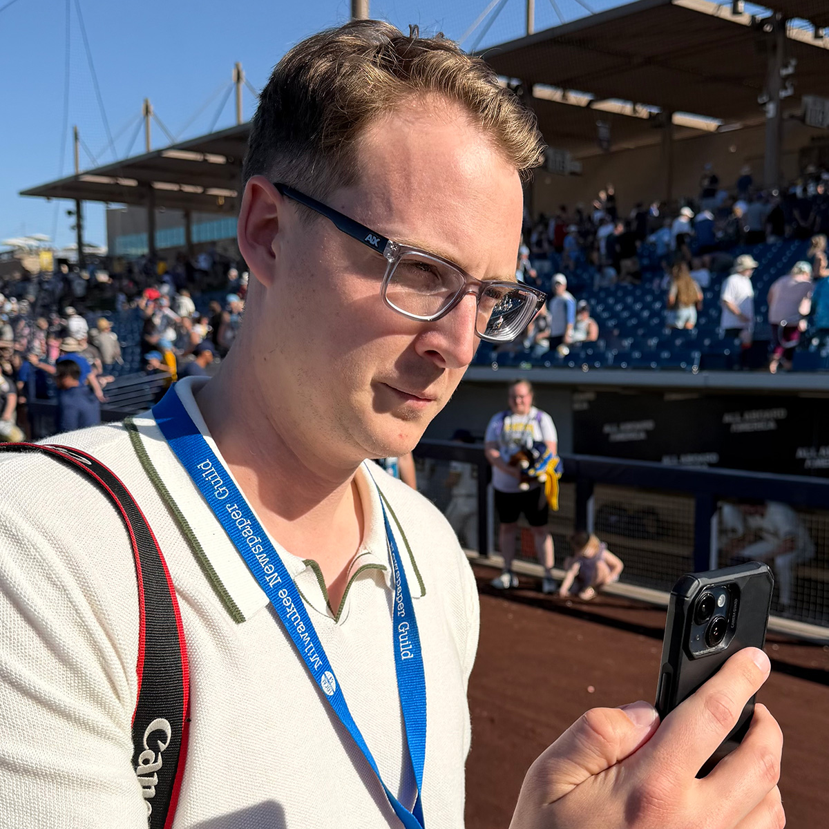 Curt Hogg looking at his phone with baseball stands in the background