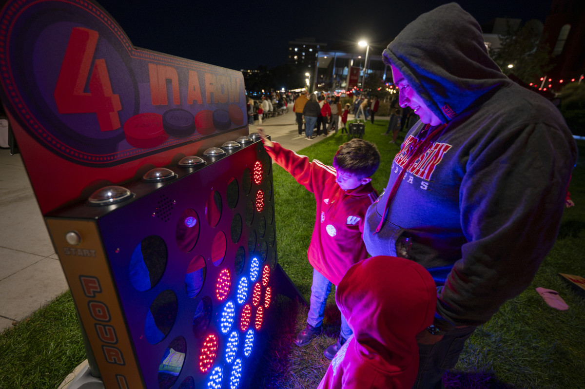 A man watches his two children play a jumbo-sized brightly-lit electronic game of Four in a Row.