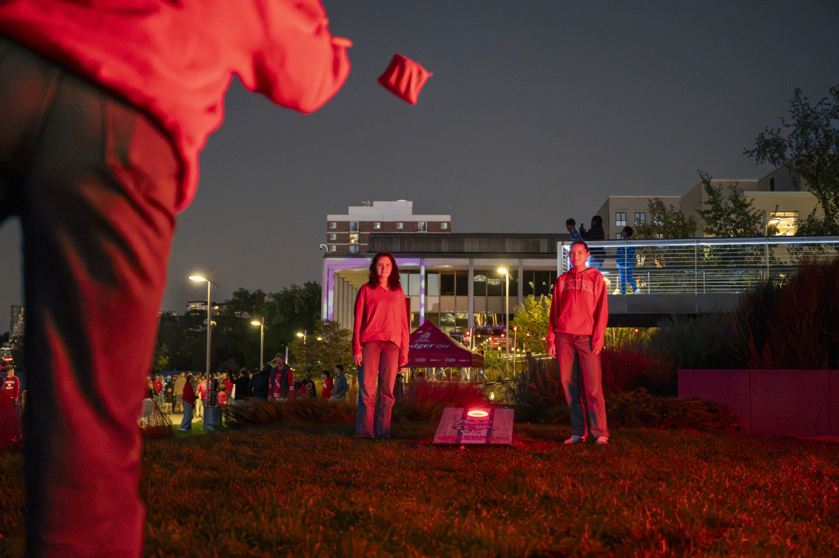 Three people stand on a grassy area of The Memorial Union Terrace to play a game of corn hole.