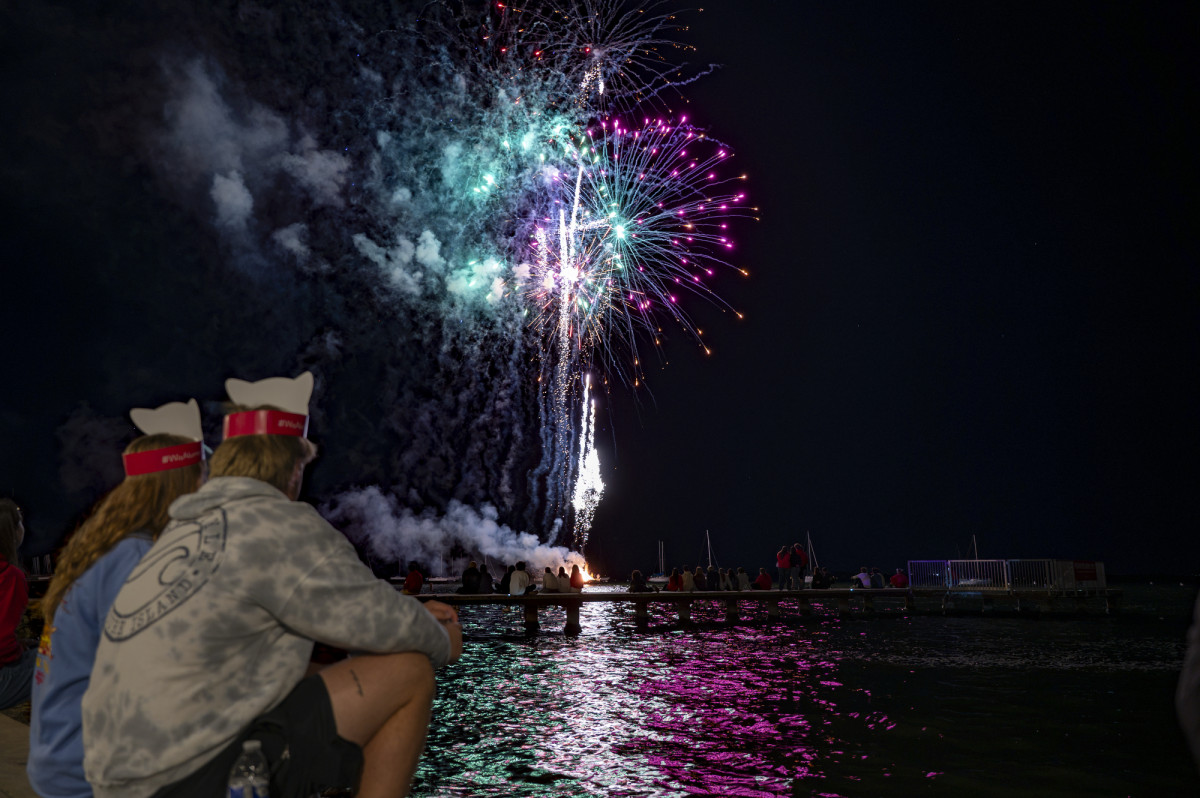 Two people wearing Bucky Badger hats watch on as fireworks explode over Lake Mendota.