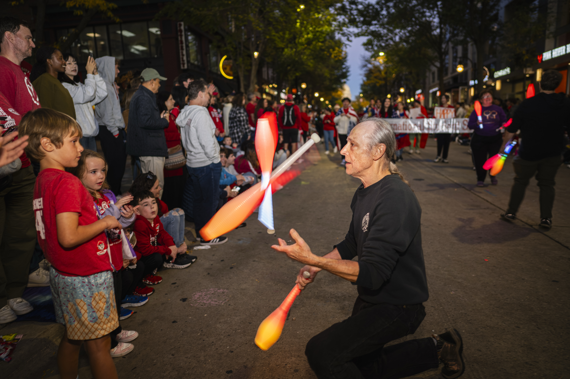 A man juggles brightly-lit juggling batons in front of mesmerized Badger fans during the UW Homecoming Parade.
