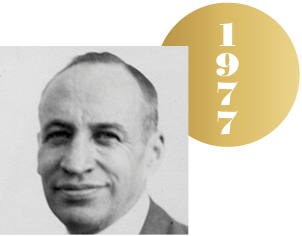 Black and white headshot of John Van Vleck with an overlapping gold circle representing a Nobel medal, with the year 1977 on it.