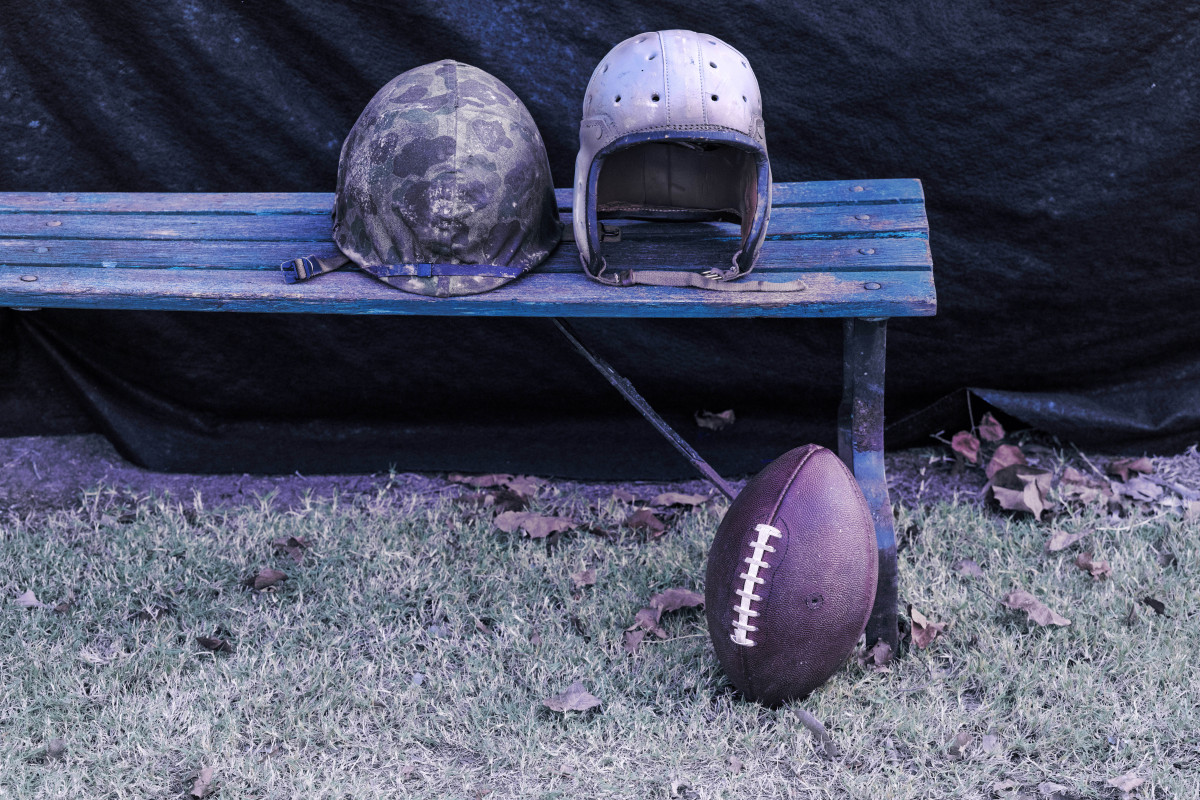 A World War Two helmet sits on a bend next to a vintage football helmet. On the ground lies a football.