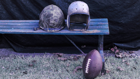 A World War Two helmet sits on a bend next to a vintage football helmet. On the ground lies a football.
