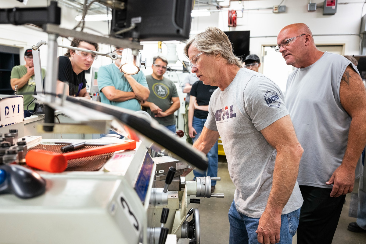 A man stands over a lathe tool while fellow METAL bootcamp participants look on while he practices using the machine.