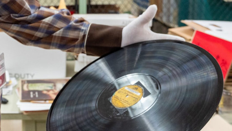 A man wears white gloves and holds an old record in his hands.