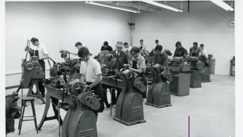 A black and white photograph shows students working at machine tooling stations.