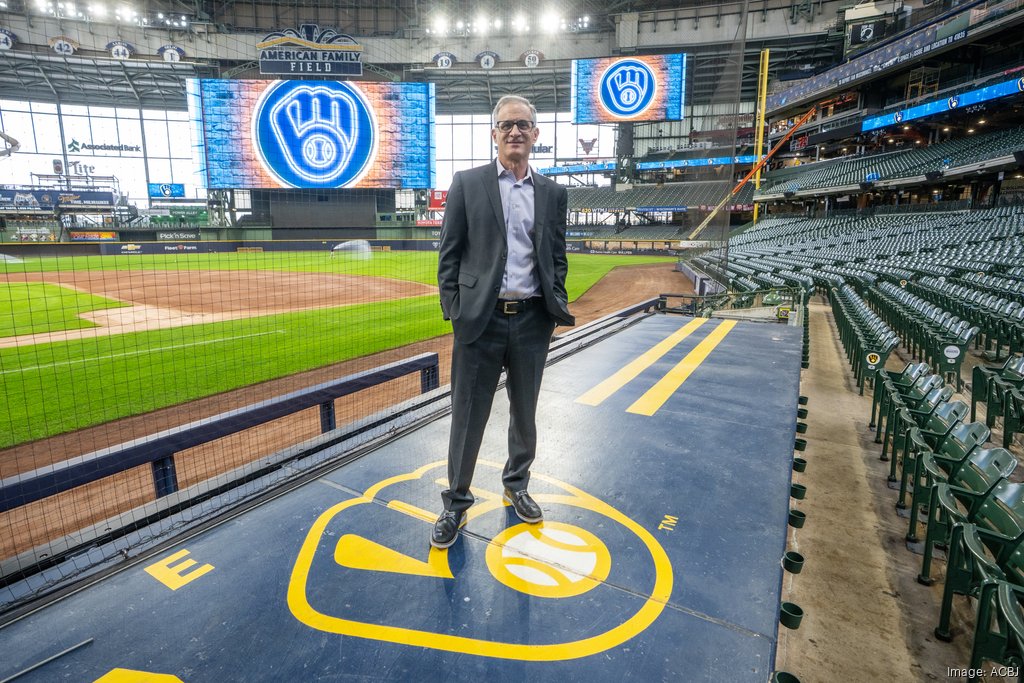 Rick Schlesinger standing on top of the Brewers dugout inside a stadium with a baseball field in the background
