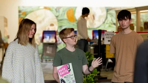 Three people stand in front of a brightly designed area. One holds a sign that reads vote early.