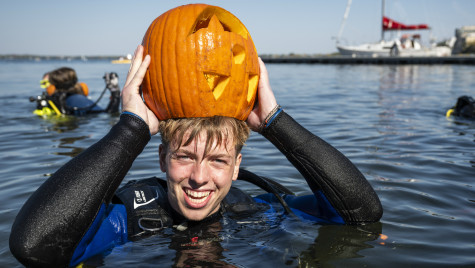 A student floats in the water and wears his carved pumpkin over his head like a hat.
