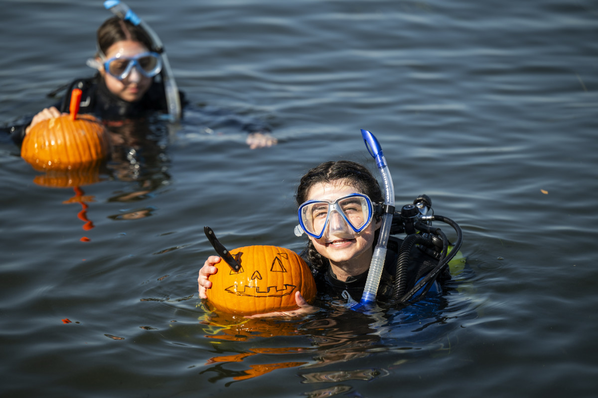 A student wearing SCUBA goggles floats in the water and holds up her not-yet-carved pumpkin for a picture.