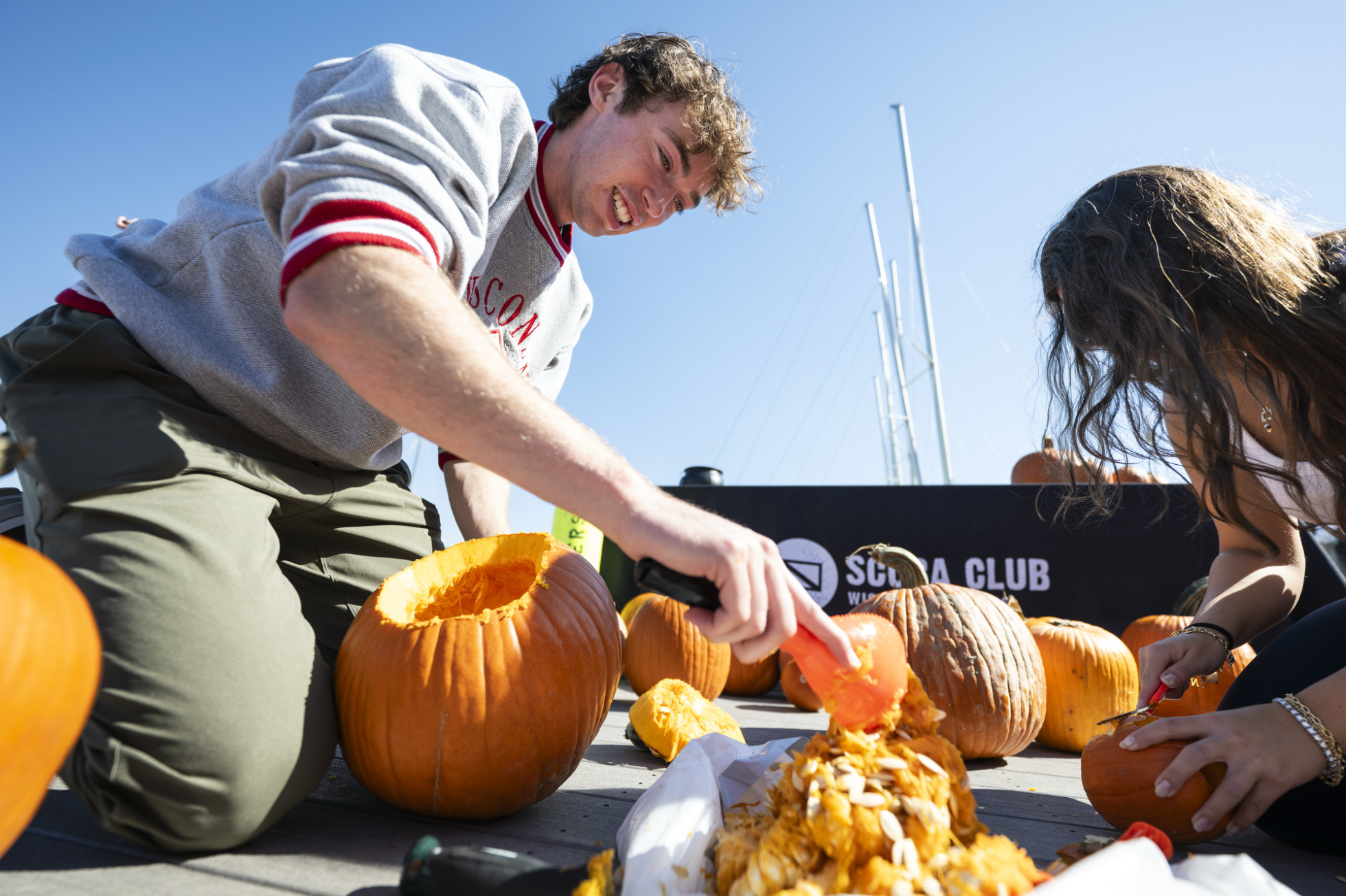 Two students kneel on the Hoofers pier on Lake Mendota to scoop the seeds from the insides of pumpkins.