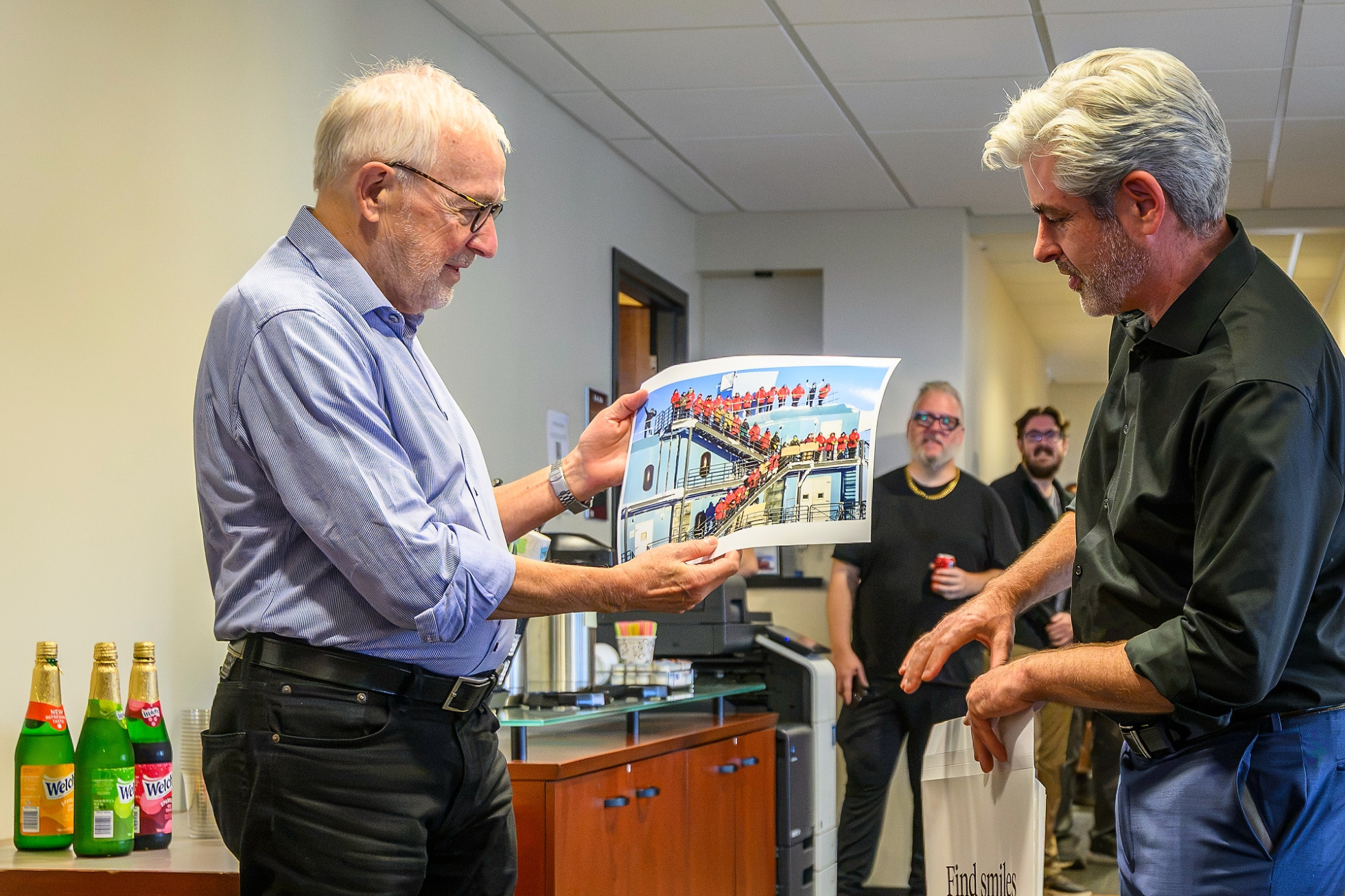 Francis Halzen holds up a printed photograph of the IceCube observatory, with a colleague next to him. 