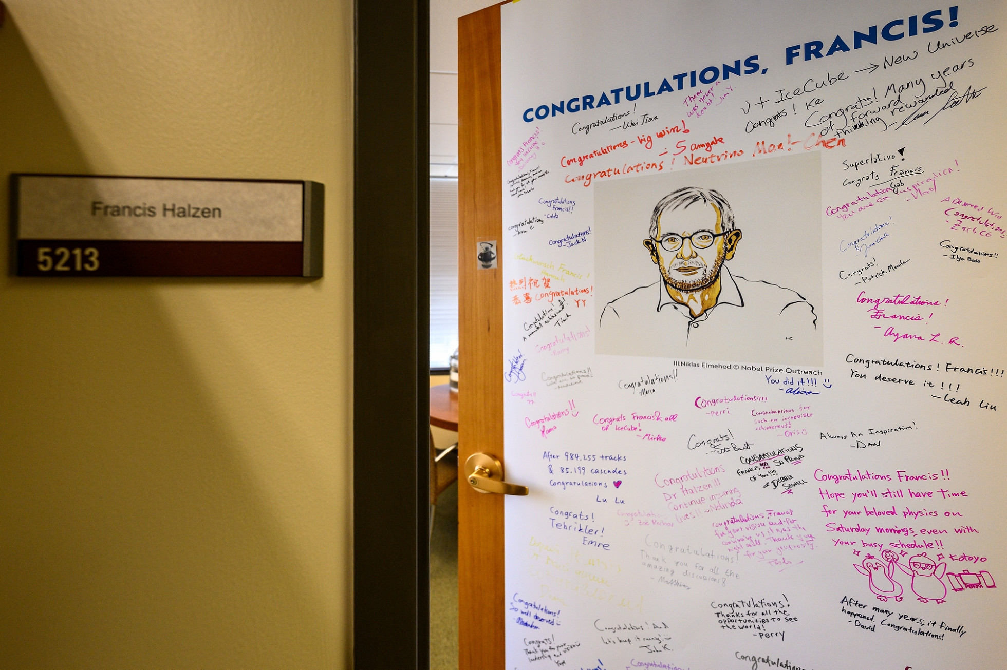 Francis Halzen's office door is shown with a large poster and hand-written notes from colleagues.