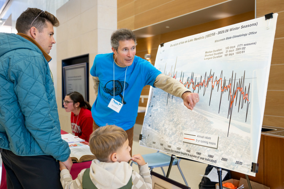 Speaking with a father holding the hand of a young child, Vavrus points to a line chart showing declining ice levels on Lake Mendota