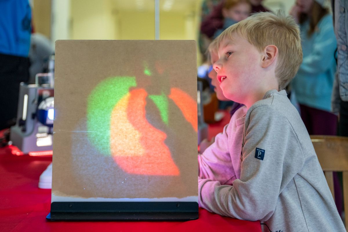 A young boy holds up a light to a projector which displays the light's rays into different colors.